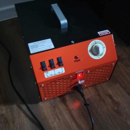 Progrix Patryk Podlipny - Pomarańczowo-czarny generator ozonu z włączonymi przełącznikami i podłączonym kablem zasilającym, ustawiony na drewnianej podłodze. Produkt Polski.