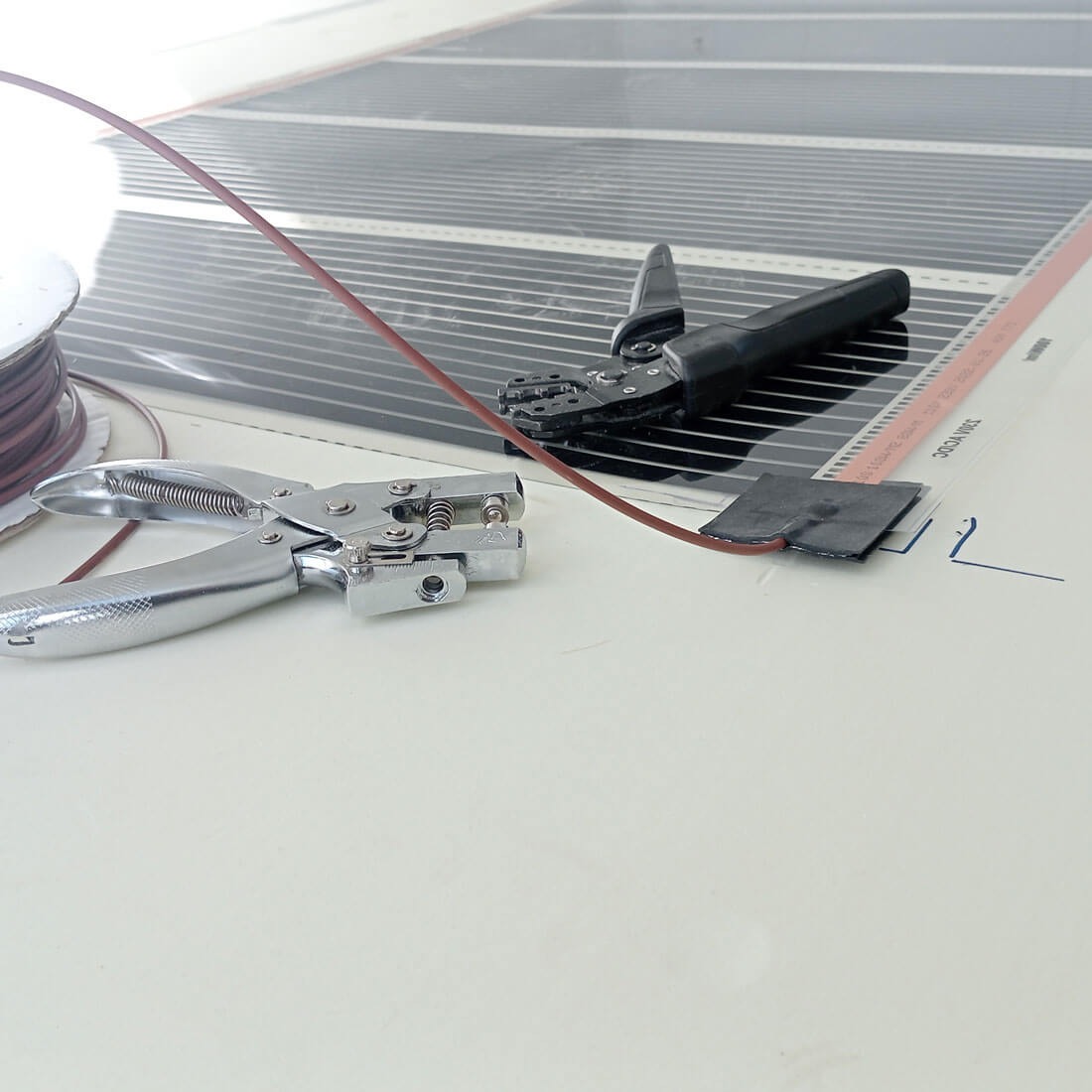 Mata grzewcza z narzędziami: zaciskarka i dziurkacz, brązowy przewód. Widok z góry na etapie montażu, detale połączeń.