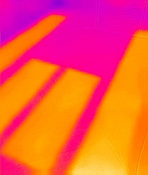 Termowizja podłogi z widocznymi, ciepłymi pasami grzewczymi w odcieniach pomarańczy i różu, ukazująca równomierne rozprowadzenie ciepła w systemie ogrzewania podłogowego.