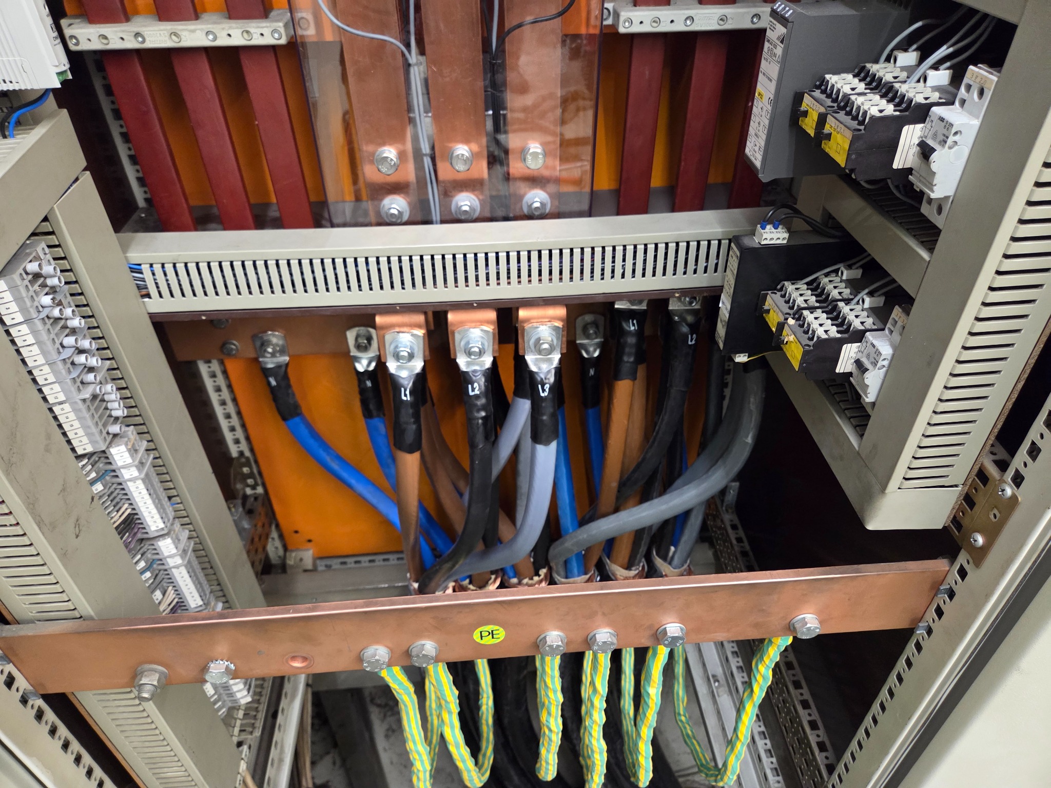 Rozdzielnica elektryczna z widocznymi przewodami, szynami miedzianymi i elementami zabezpieczającymi. Detal instalacji elektrycznej wewnątrz szafy sterowniczej.