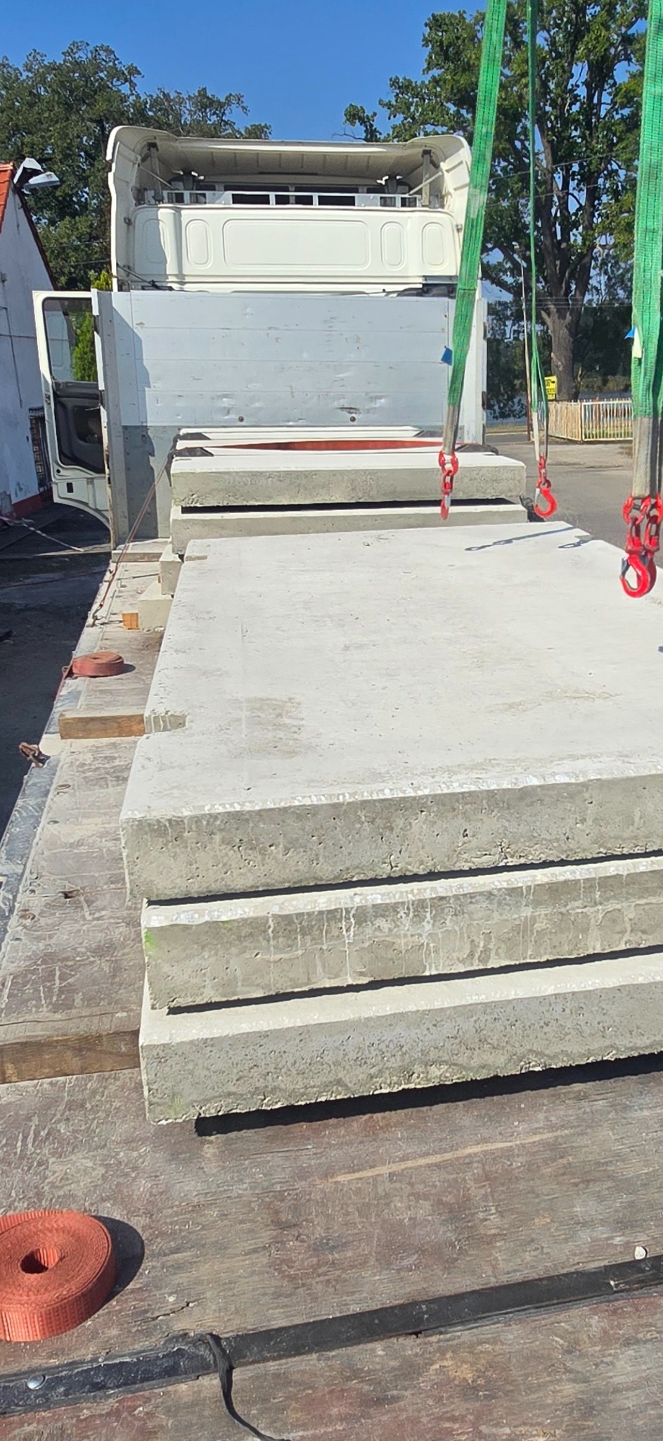 Transport betonowych płyt drogowych na ciężarówce, zabezpieczonych pasami transportowymi. Widoczne detale faktury betonu i mocowania.