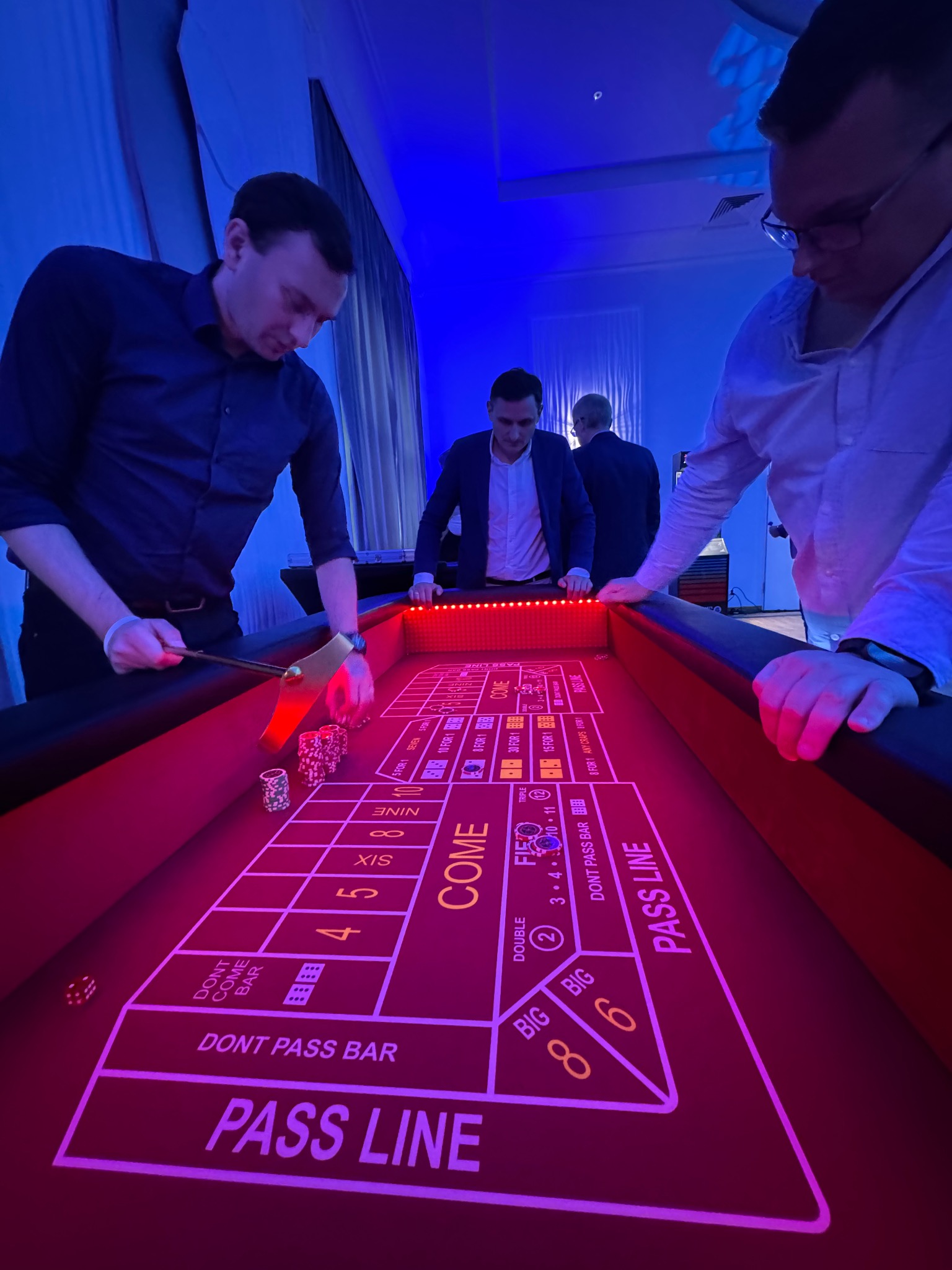 Gra w kości na imprezie firmowej: trzech mężczyzn przy stole do gry w kasynie, żetony, kostki, oświetlenie LED. Atrakcja na event.