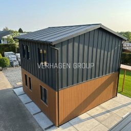 Verhagen Kraków Sp. z o. o. - Dwukondygnacyjny dom modułowy z szarej blachy falistej i brązowych paneli, widok z góry, z logo firmy na elewacji. Nowoczesna architektura.