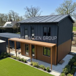 Verhagen Kraków Sp. z o. o. - Dwukondygnacyjny dom modułowy z szarej blachy trapezowej i drewnianą werandą, otoczony zielenią. Widok z góry, w tle inne budynki i drzewa.