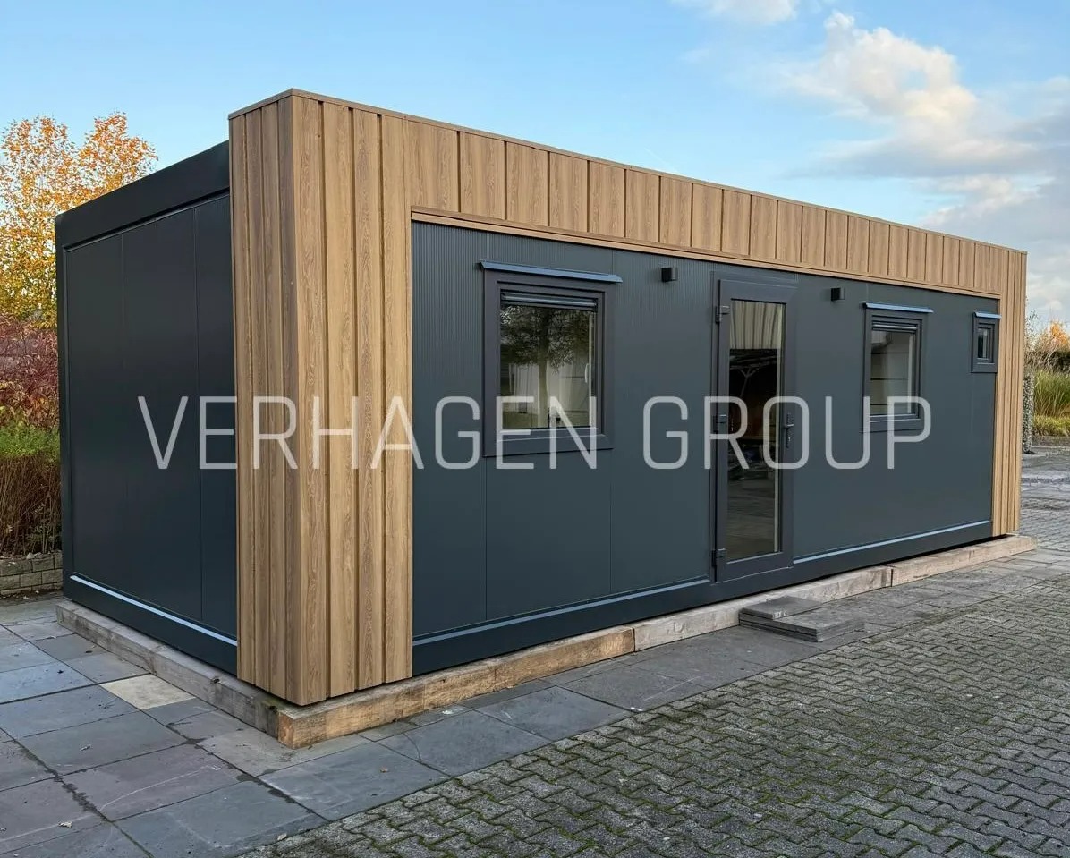 Nowoczesny dom modułowy z szarymi panelami i drewnianymi akcentami, widoczny z zewnątrz na tle błękitnego nieba. Minimalistyczny design z oknami i przeszklonymi drzwiami.