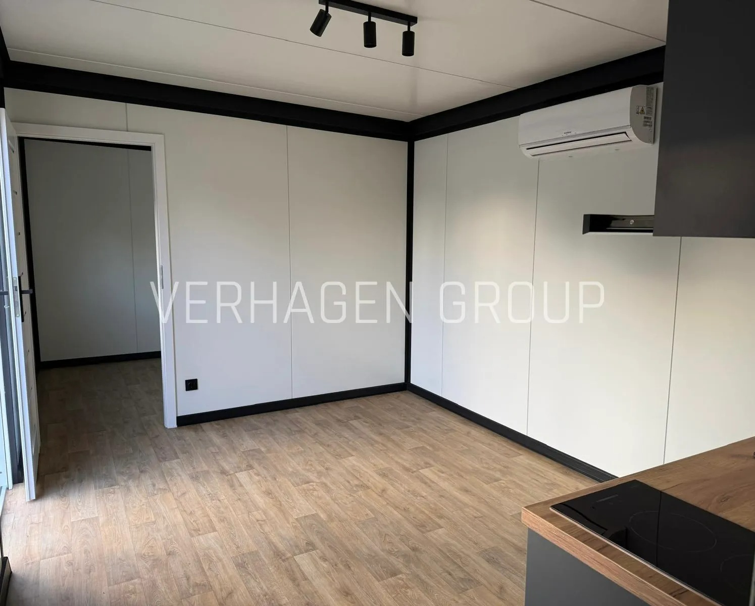 Wnętrze modułowego domu z klimatyzacją, oświetleniem punktowym i wykończoną podłogą. Widoczny fragment zabudowy kuchennej z płytą indukcyjną.