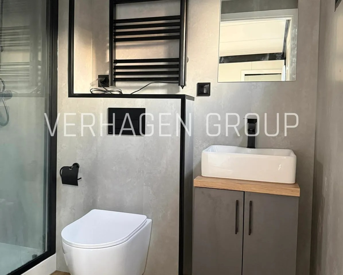 Nowoczesna łazienka w szarościach: podwieszana toaleta, umywalka nablatowa na szafce, czarny grzejnik drabinkowy i minimalistyczne dodatki. Wykończenie w stylu loftowym.