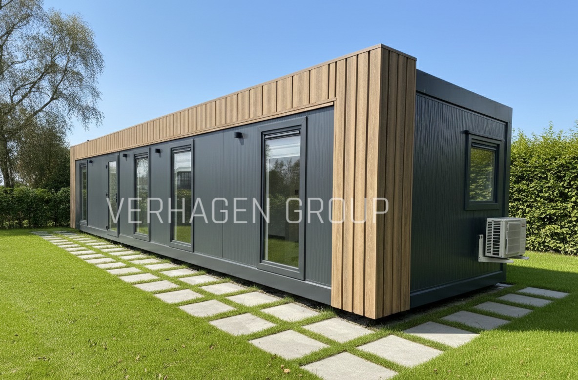 Nowoczesny dom modułowy z szarymi panelami i drewnianymi akcentami, otoczony zielonym trawnikiem i ścieżką z płyt. Widoczny klimatyzator na bocznej ścianie.