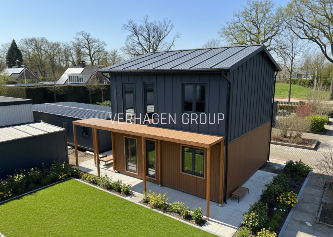 Dwukondygnacyjny dom modułowy z szarej blachy trapezowej i drewnianą werandą, otoczony zielenią. Widok z góry, w tle inne budynki i drzewa.