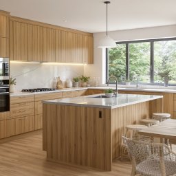 AMP INWESTYCJE SPÓŁKA Z OGRANICZONĄ ODPOWIEDZIALNOŚCIĄ - Jasna kuchnia z drewnianymi frontami, wyspą i marmurowym blatem. Nowoczesne oświetlenie, okno z widokiem na zieleń. Stół z plecionymi krzesłami.