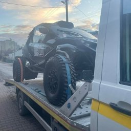 Pomoc w Trasie - pomoc drogowa, laweta, transport, awaryjne uruchamianie Częstochowa - Czarny pojazd terenowy z numerem 810, zabezpieczony pasami, przewożony na platformie lawety na tle miejskiej ulicy w pochmurny dzień.