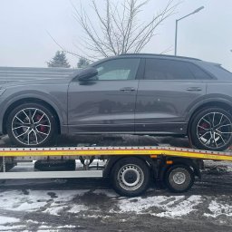 Pomoc w Trasie - pomoc drogowa, laweta, transport, awaryjne uruchamianie Częstochowa - Szary SUV Audi Q8 na żółtej platformie lawety, widok z boku, zimowa sceneria. Czerwone zaciski hamulcowe za felgami.