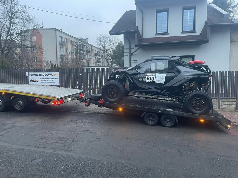 Czarny pojazd terenowy typu buggy z numerem 810, zabezpieczony na niskopodwoziowej lawecie, z widocznym budynkiem mieszkalnym w tle.