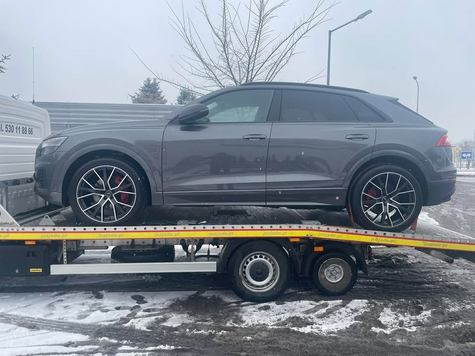 Szary SUV Audi Q8 na żółtej platformie lawety, widok z boku, zimowa sceneria. Czerwone zaciski hamulcowe za felgami.