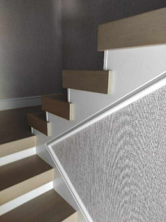 Nowoczesne schody z jasnego drewna i białymi elementami, widok z dołu, z bliska. Minimalistyczny design, szara ściana w tle.