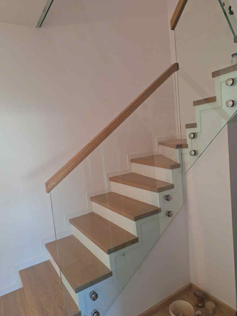 Nowoczesne schody drewniane z balustradą szklaną, drewniany pochwyt, białe stopnie, minimalistyczny design, widok z dołu, jasne wnętrze.