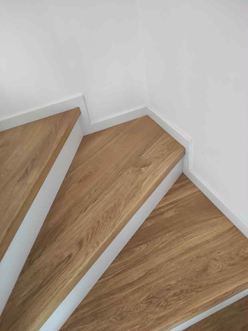 Fragment drewnianych schodów z białymi podstopnicami, widok z góry, ukazujący naturalny rysunek drewna i minimalistyczne wykończenie.