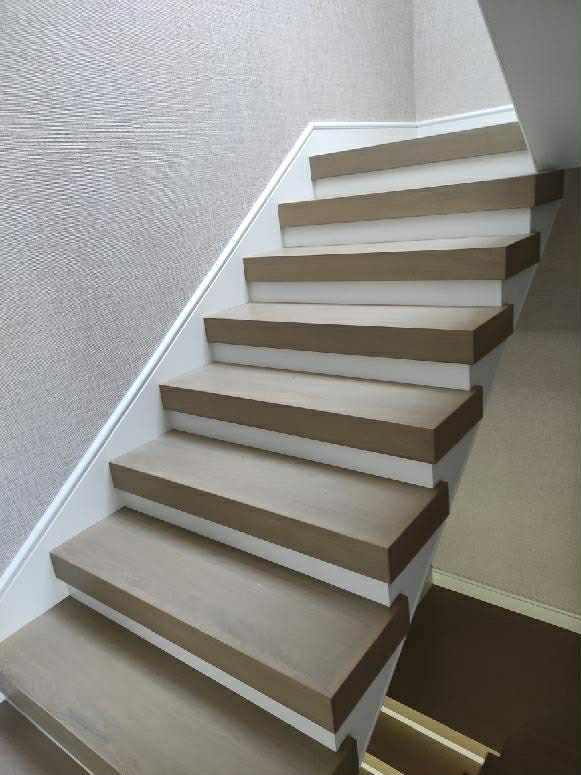 Nowoczesne schody z drewnianymi stopniami i białymi podstopnicami, widok z dołu, jasne wnętrze, minimalistyczny design.