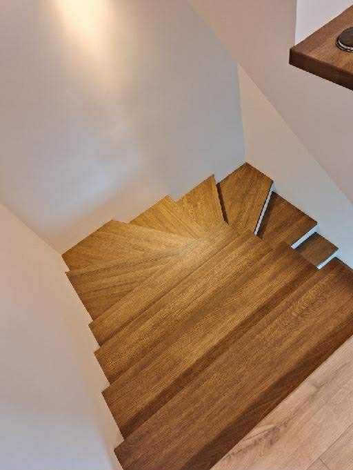 Kaskada stopni z egzotycznego drewna, widok z góry. Naturalne wykończenie, ciepłe oświetlenie akcentuje rysunek słojów. Minimalistyczne wnętrze.