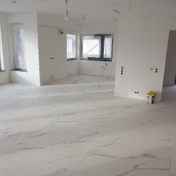 PORTAL Maciej Hyżowiecki - Jasne, marmurowe płytki podłogowe w przestronnym, surowym wnętrzu. Okna zabezpieczone folią, ściany przygotowane do malowania, widoczne puszki elektryczne.