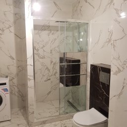 PORTAL Maciej Hyżowiecki - Wykończona łazienka z kabiną prysznicową, toaletą podwieszaną i pralką. Płytki imitujące marmur na ścianach i podłodze. Nowoczesny design.