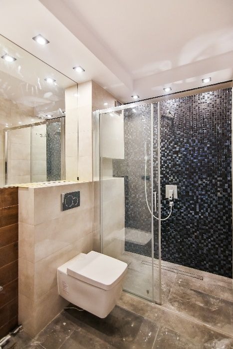 Nowoczesna łazienka z kabiną prysznicową wyłożoną mozaiką w odcieniach szarości i czerni. Podwieszana toaleta, beżowe płytki ścienne i sufitowe oświetlenie punktowe.