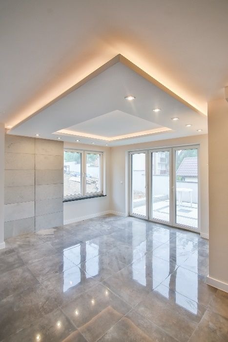 Jasne wnętrze z szarą, marmurkową podłogą, dekoracyjną ścianą z paneli i podwieszanym sufitem z oświetleniem LED. Nowoczesny design, duże okna.