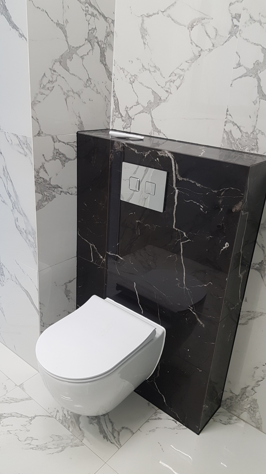 Nowoczesna toaleta podwieszana z czarną obudową i marmurowymi płytkami na ścianach i podłodze. Minimalistyczny design, eleganckie wykończenie.