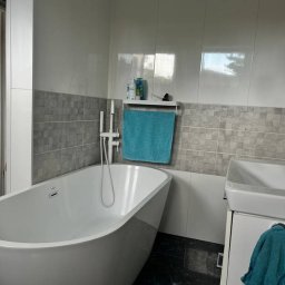 Stanisław Kach - Nowoczesna łazienka z wolnostojącą wanną, szarymi płytkami i turkusowymi akcentami. Minimalistyczny design, czarne płytki podłogowe, schludne wykończenie.