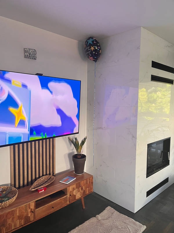Salon z marmurową ścianą kominkową, drewnianą szafką RTV i telewizorem. Uwagę przykuwa balon z gwiazdkami, dodający wnętrzu radosnego charakteru.