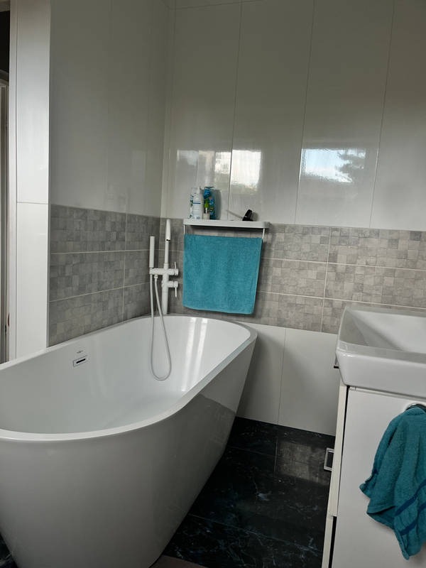 Nowoczesna łazienka z wolnostojącą wanną, szarymi płytkami i turkusowymi akcentami. Minimalistyczny design, czarne płytki podłogowe, schludne wykończenie.