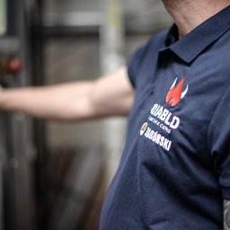 Agencja Marketingowa APOV - Mężczyzna w granatowej koszulce polo z logo firmy 'Diablo' i tatuażem na ramieniu, obsługujący maszynę. Widoczne detale logo i fragment panelu sterowania.