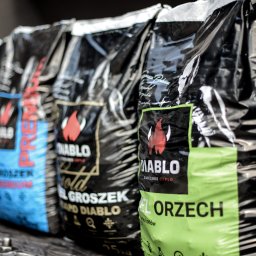 Agencja Marketingowa APOV - Rząd worków węgla marki Diablo, każdy w innym kolorze (czerwony, niebieski, czarny, zielony), z widocznym logo płomienia i nazwą produktu. Ustawione na metalowej powierzchni.