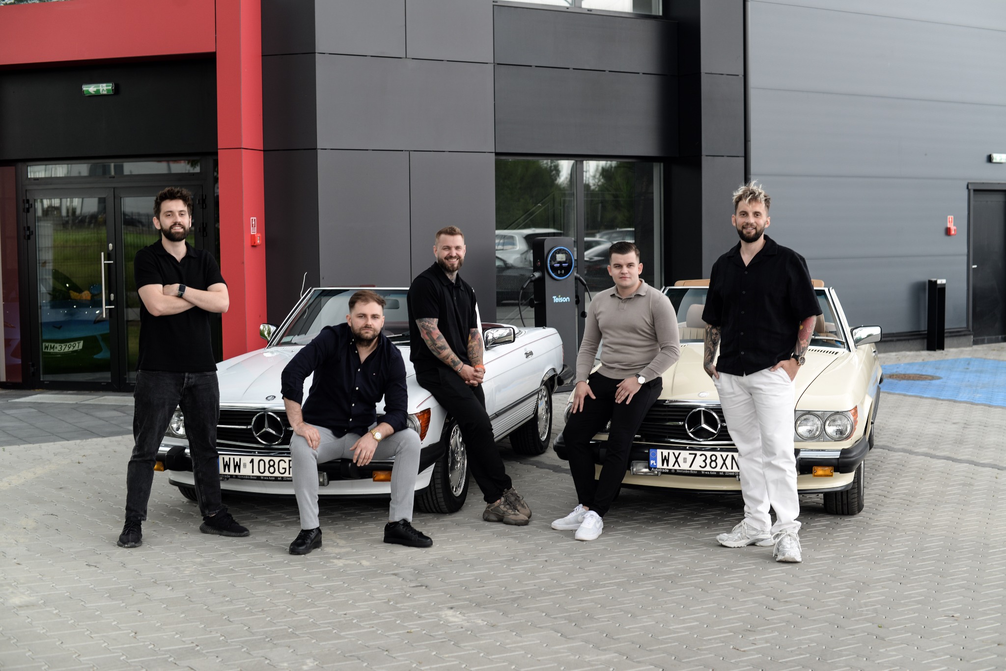 Grupa pięciu mężczyzn pozuje przed dwoma zabytkowymi Mercedesami SL w nowoczesnym otoczeniu z ładowarką Teison, tworząc unikalną sesję biznesową.