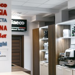 Coffee Cona Marcin Ostrówka - Ekspozycja ekspresów do kawy różnych marek (Saeco, Gaggia, Jura, Philips, Delonghi) w salonie sprzedaży. Widoczne modele domowe i gastronomiczne na półkach.
