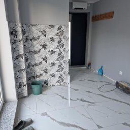 Usługi Budowlane Damian Borys - Wykończone wnętrze z marmurową podłogą i wzorzystą okładziną ściany. Widoczne narzędzia i akcesoria malarskie. Nowoczesne oświetlenie sufitowe.