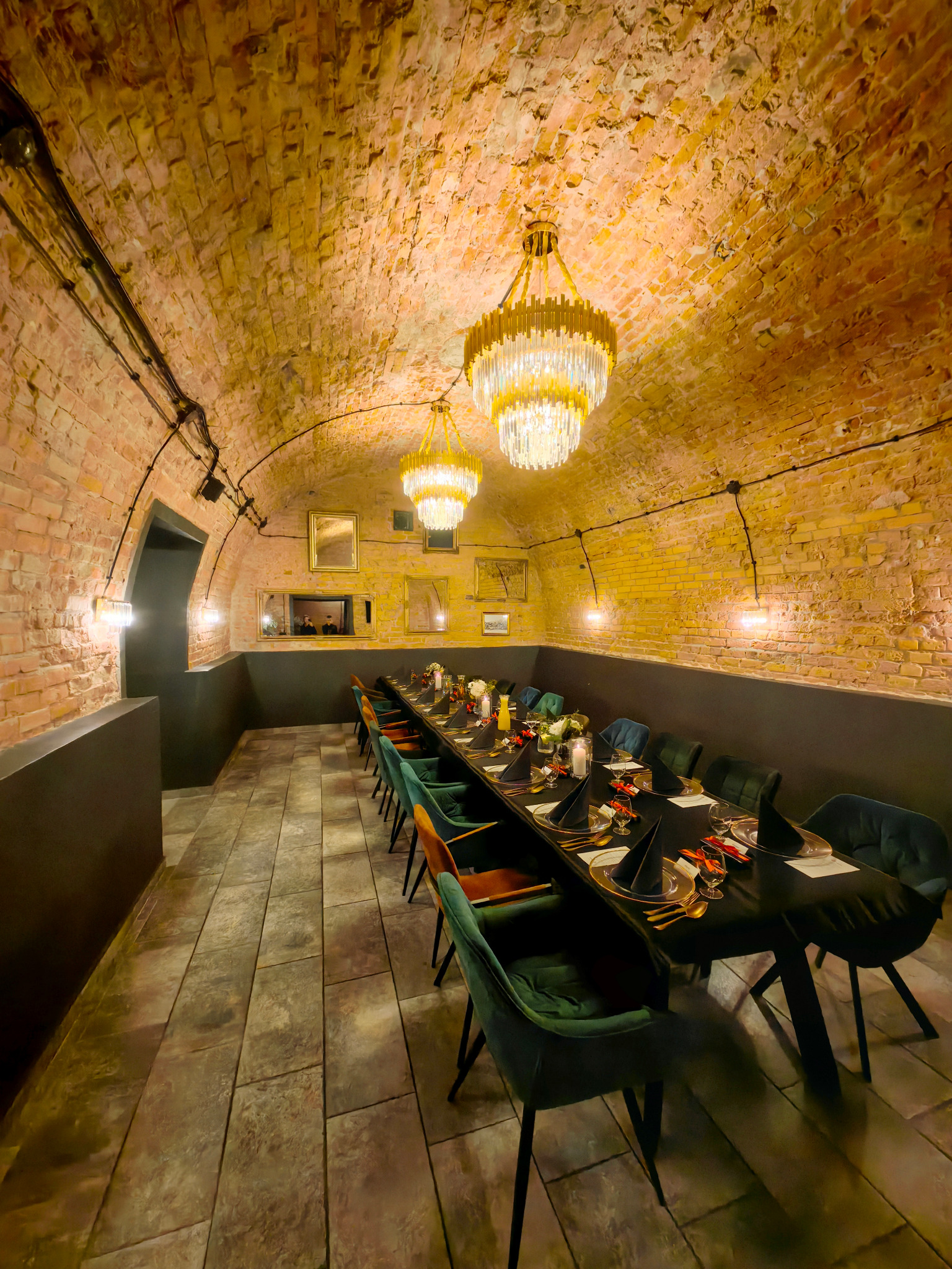 Uroczysta aranżacja stołu w ceglanym wnętrzu z kryształowymi żyrandolami. Czarny obrus, elegancka zastawa i kolorowe krzesła tworzą wyjątkowy klimat.