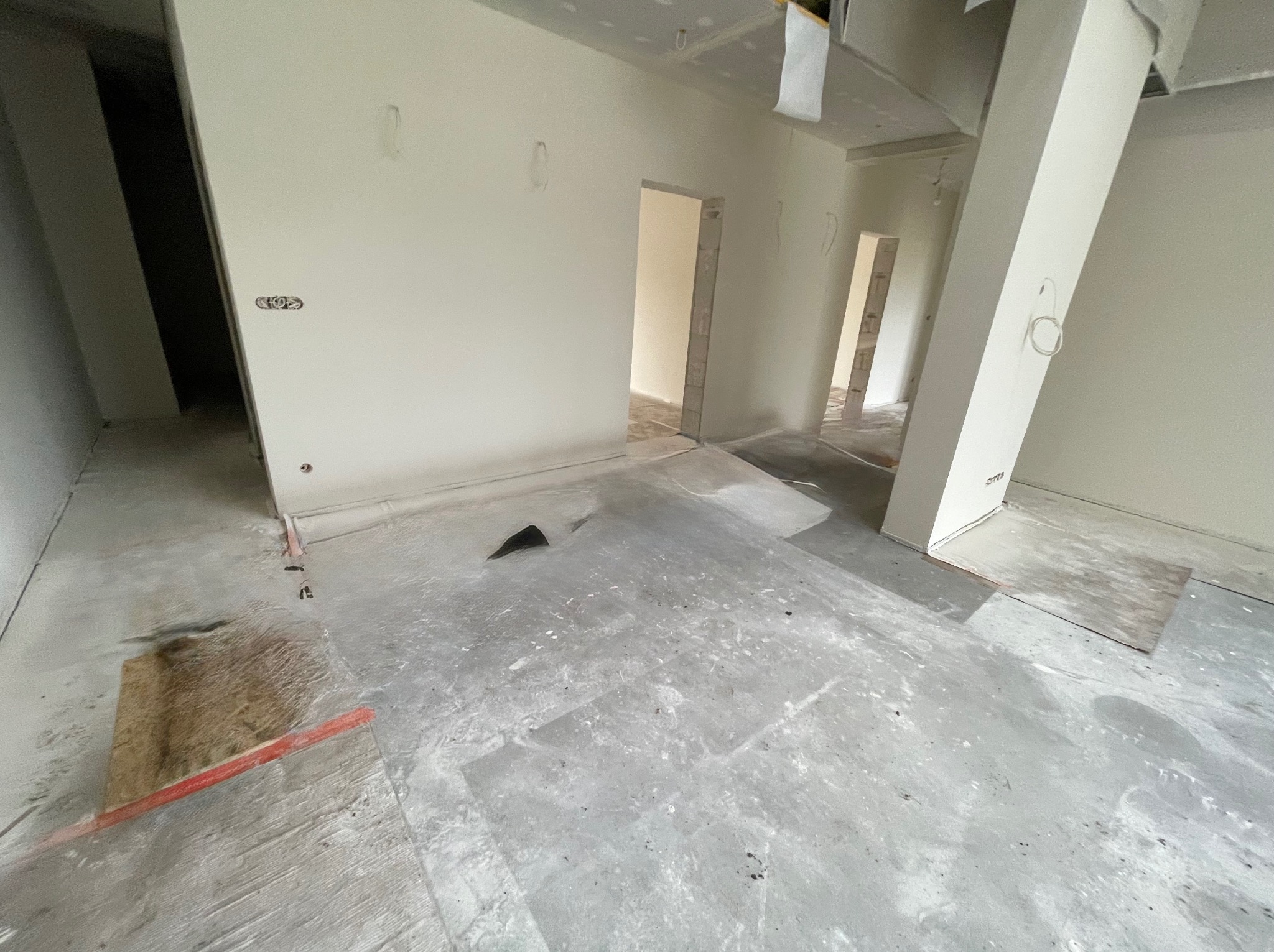 Wnętrze w trakcie prac wykończeniowych: ściany przygotowane pod malowanie, widoczne ślady po szpachlowaniu, surowa podłoga. W tle widoczne otwory drzwiowe.