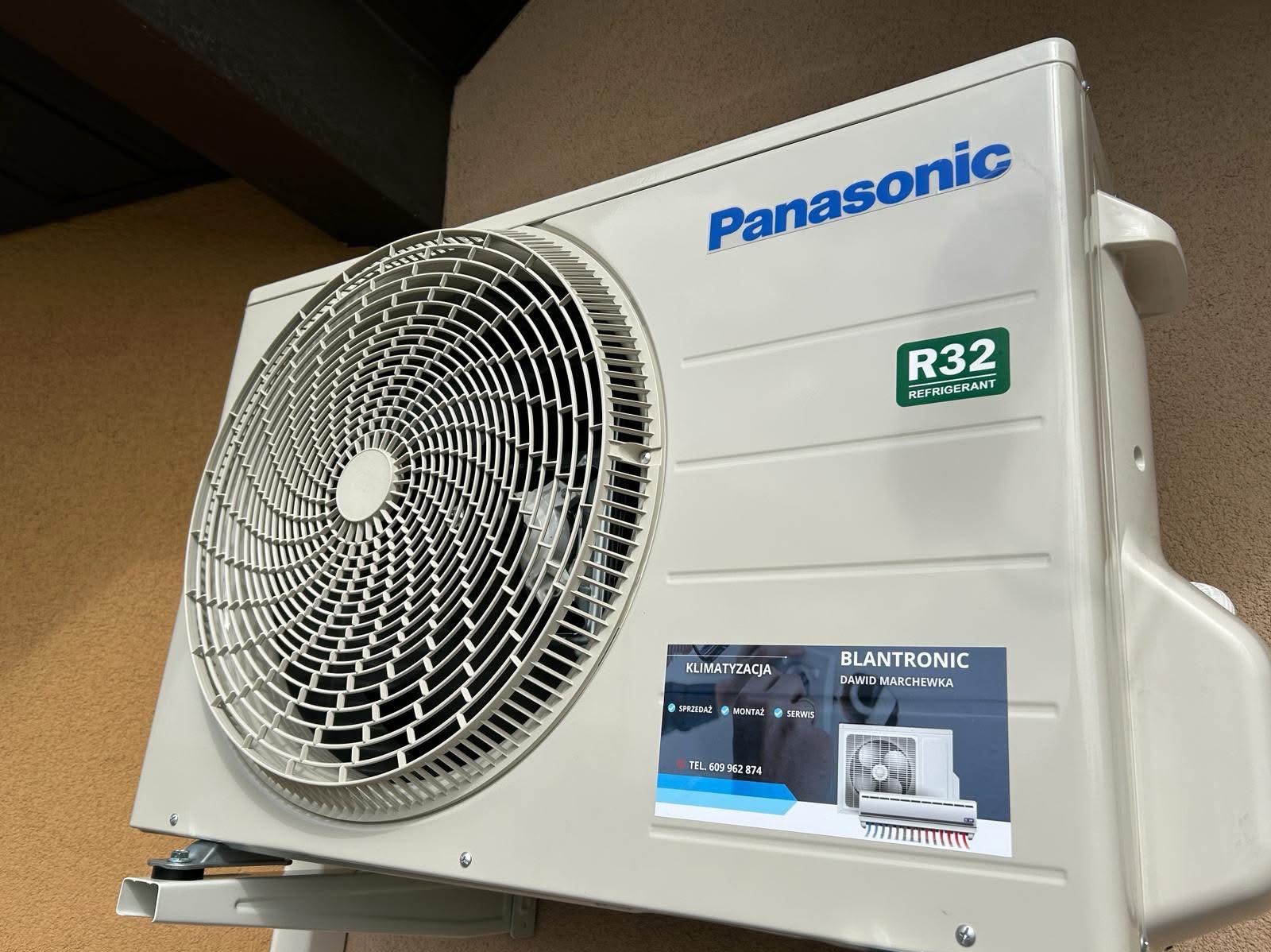 Zamontowana jednostka zewnętrzna klimatyzacji Panasonic z widoczną naklejką firmy Blantronic oferującej sprzedaż, montaż i serwis klimatyzacji.