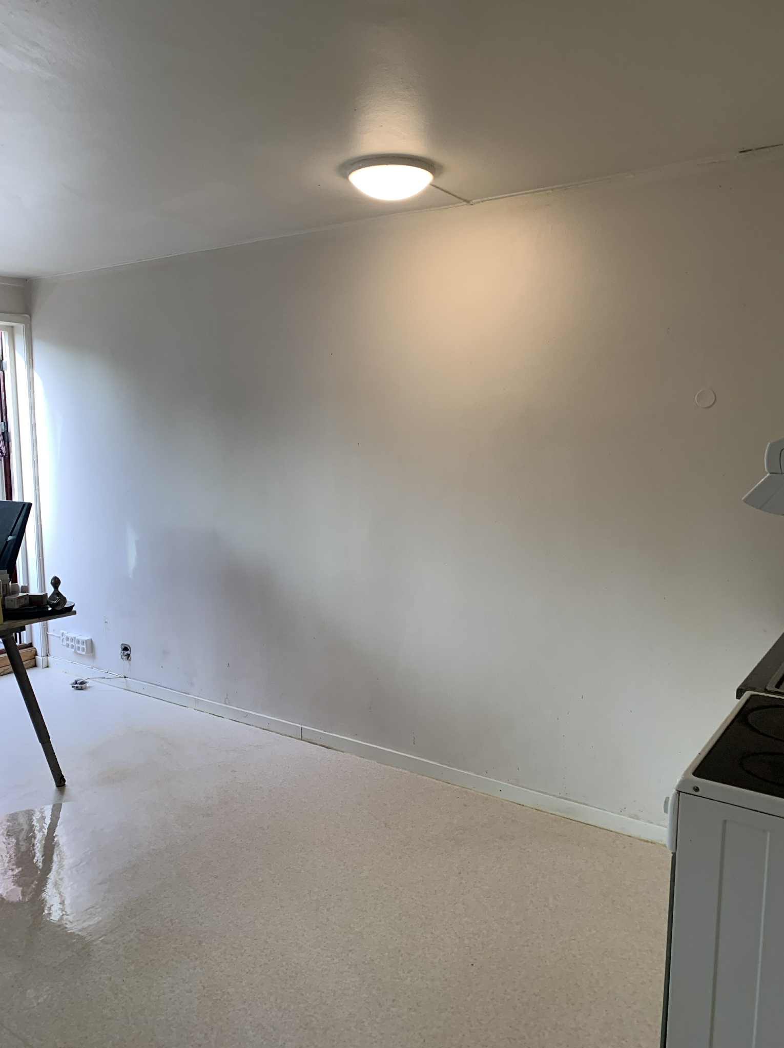 Jasne wnętrze po sprzątaniu: błyszcząca podłoga, czyste ściany i sufit z lampą. Widoczny fragment kuchenki i stolika. Minimalistyczny wystrój, świeżość i porządek.