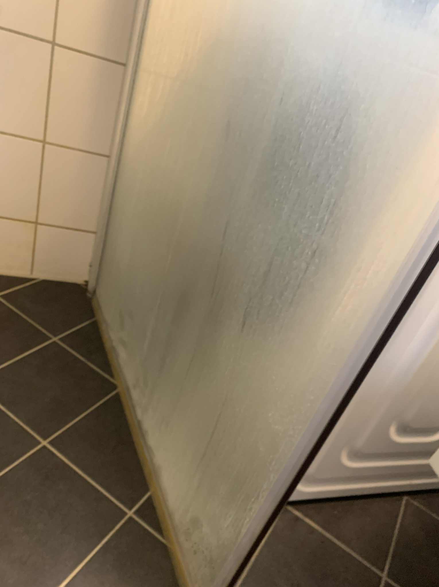 Zabrudzona kabina prysznicowa z widocznymi zaciekami i osadem, narożnik z ciemnymi płytkami podłogowymi i jasnymi płytkami ściennymi w tle.