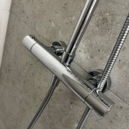 PowerClean - Błyszcząca, chromowana bateria prysznicowa Omnires zamontowana na szarej, kamiennej ścianie. Widoczne węże i głowica prysznicowa. Ujęcie z bliska, z boku.