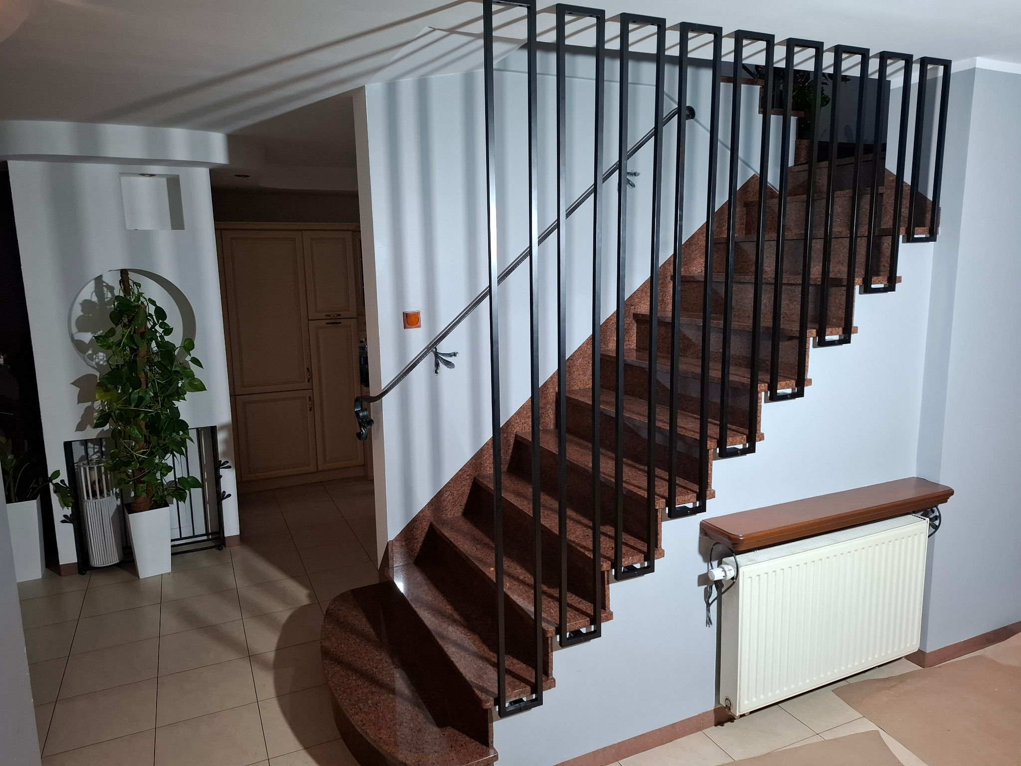 Granitowe schody z czarną, minimalistyczną konstrukcją. Ujęcie z dołu, widoczne detale wykończenia i oświetlenie wnętrza. Nowoczesny design.