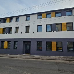 BeEcoEnergy Bartłomiej Koćwin - Odnowiona kamienica po termomodernizacji z nowoczesną elewacją w odcieniach szarości, bieli i akcentami drewna. Widok z poziomu ulicy, pochmurne niebo.