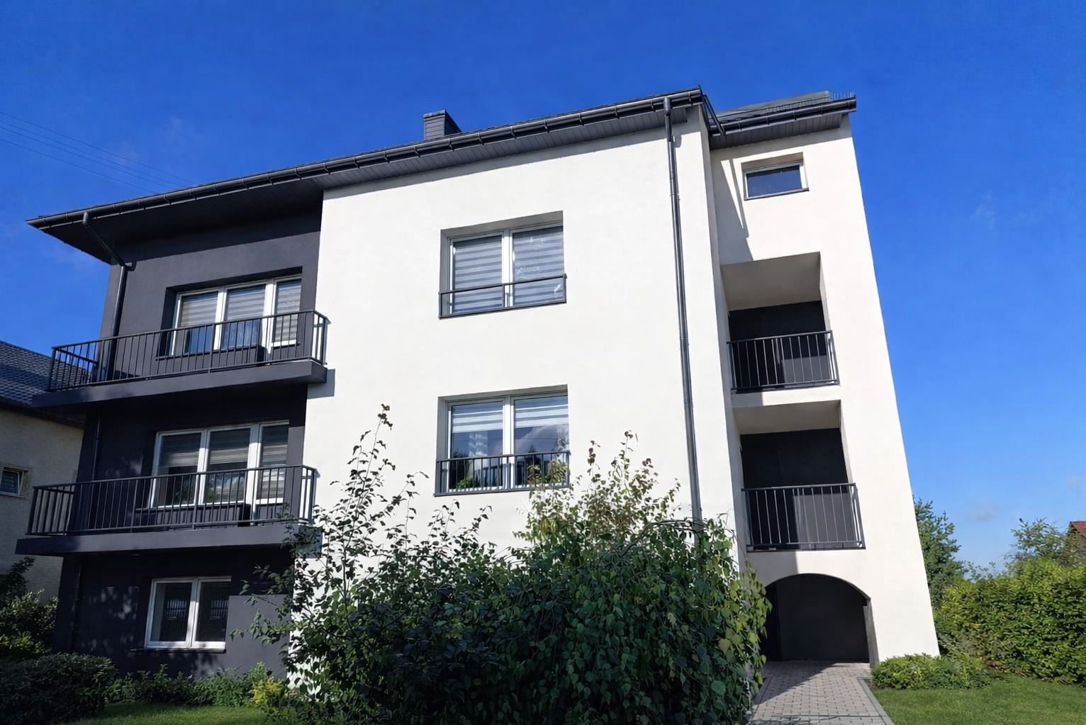 Termomodernizacja budynku w Częstochowie: styropian grafitowy 15cm, tynk silikonowy w dwóch odcieniach szarości. Widok z dołu, balkony z czarną balustradą.