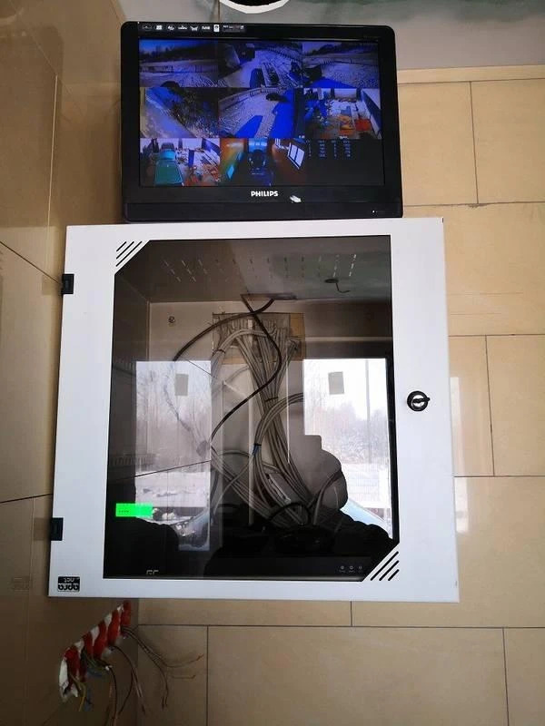 Monitor Philips z podglądem z kamer CCTV nad szafką z okablowaniem. Widoczne kable i złącza. Całość zamontowana na ścianie z płytek.
