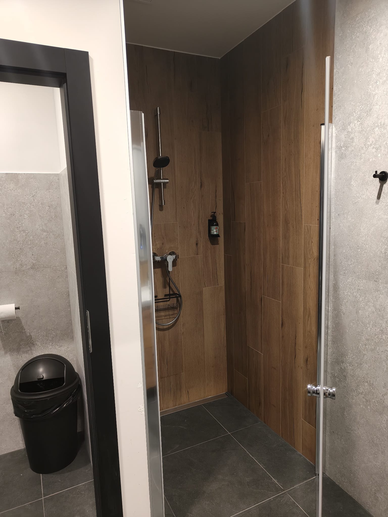 Nowoczesna kabina prysznicowa z drewnopodobnymi płytkami w Białymstoku. Szklane drzwi, szara podłoga i ściany. Minimalistyczny design.