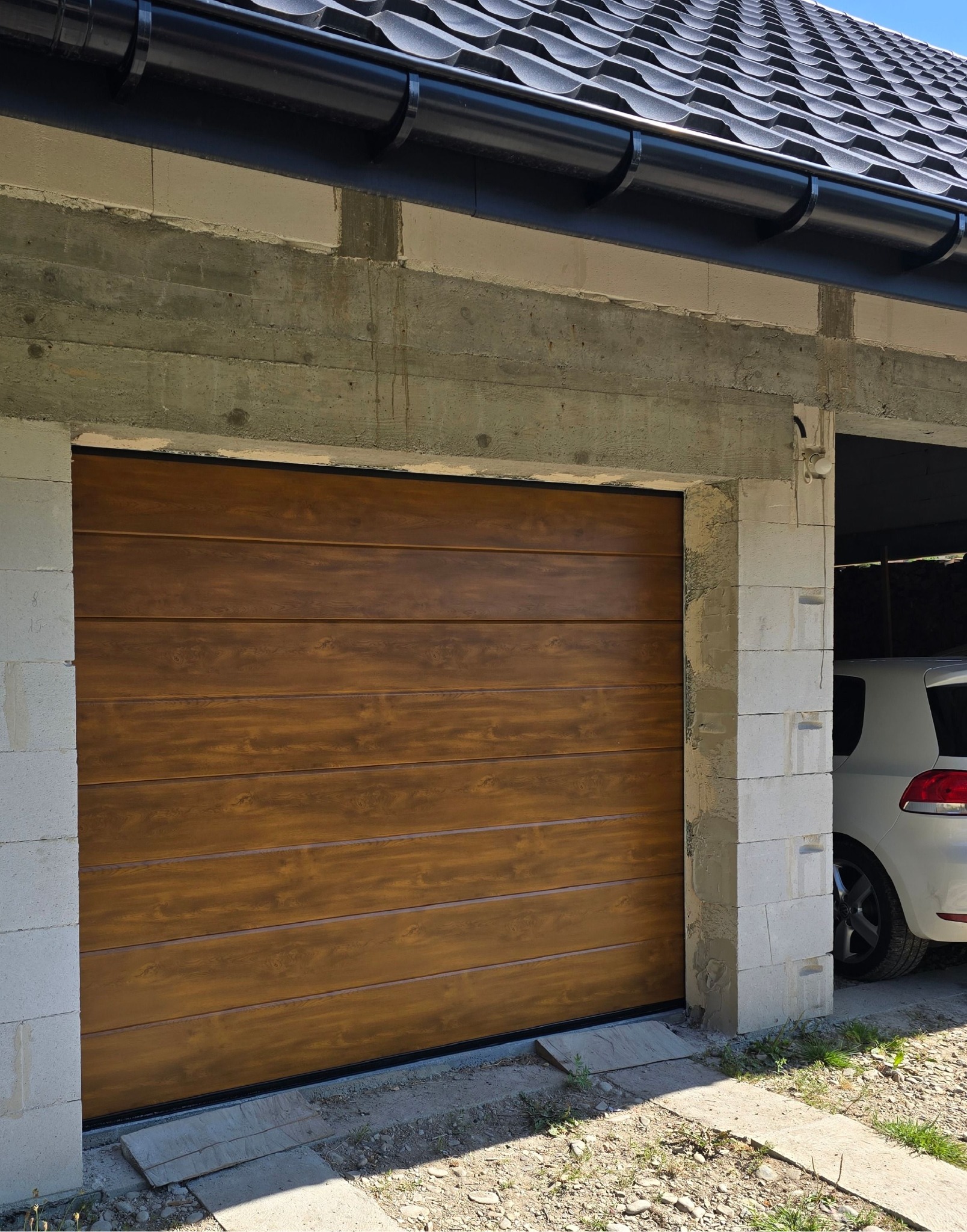 Zamknięta brama garażowa segmentowa w kolorze drewna, widoczna od zewnątrz, w surowym otoczeniu budowlanym. Usługa montażu w Krakowie.