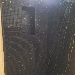 R-BAU USŁUGI REMONTOWO-BUDOWLANE ROBERT PŁOTKA - Wykończona kabina prysznicowa z czarną mozaiką i wnęką, akcentowana złotymi elementami. Obok ściana z czarnego marmuru z białymi żyłami.