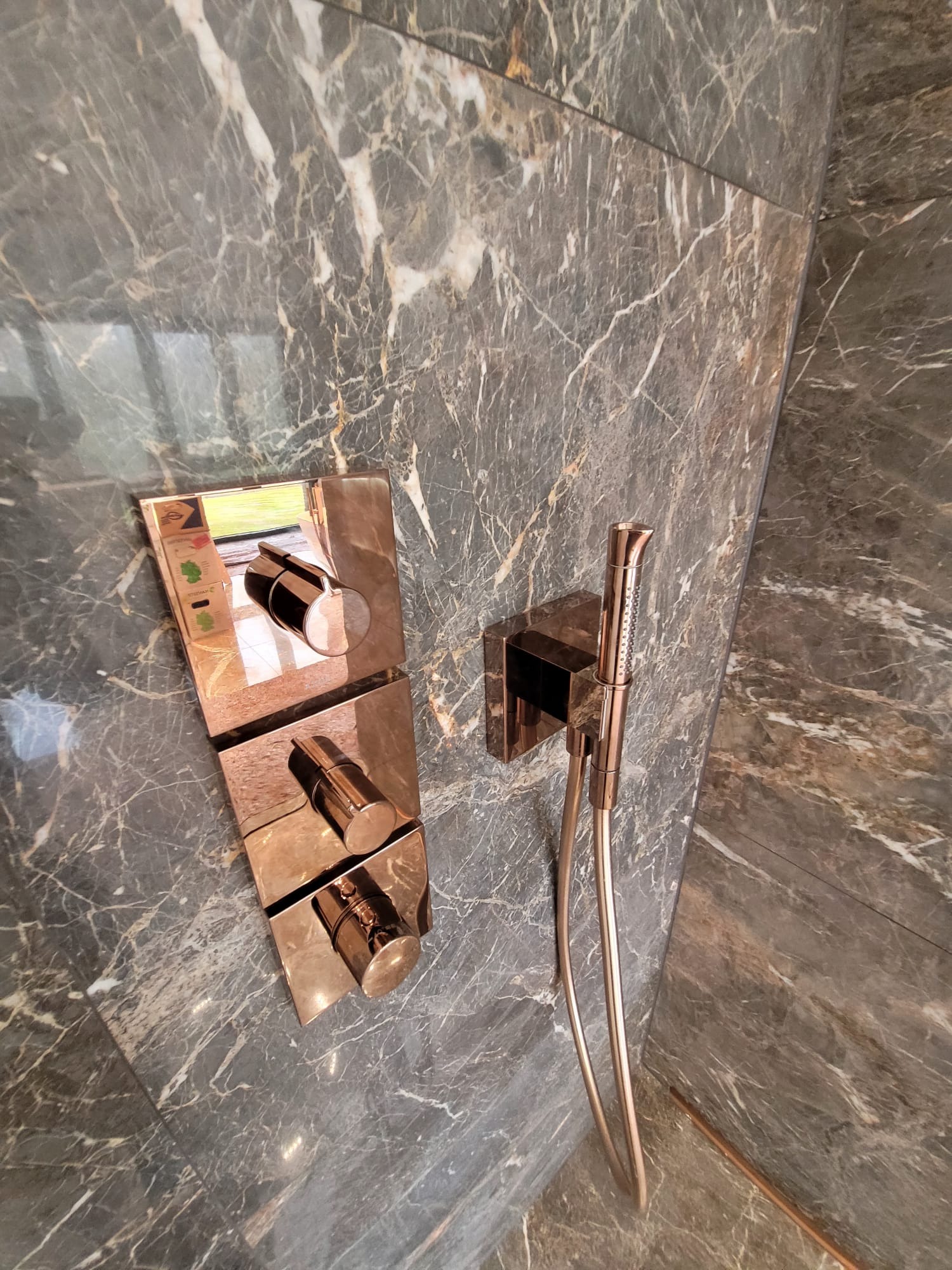 Luksusowa kabina prysznicowa z marmurowymi płytami i miedzianą armaturą: bateria z termostatem i słuchawka prysznicowa. Eleganckie wykończenie łazienki.